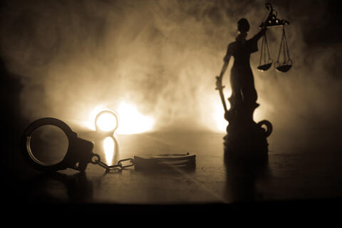 Handcuffs are laid at the feet of a statue holding the scales of justice
