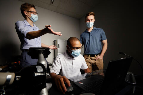 Three men crowd around a computer