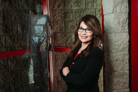 A woman in a suit leans against a stone wall