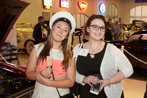 Two women stand in front of cars