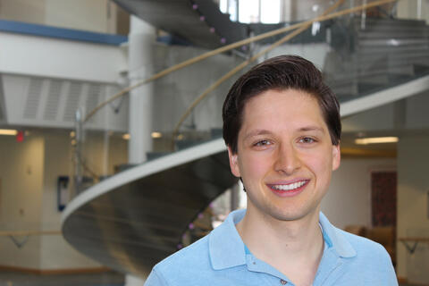 A man stands in front of  a staircase, smiling