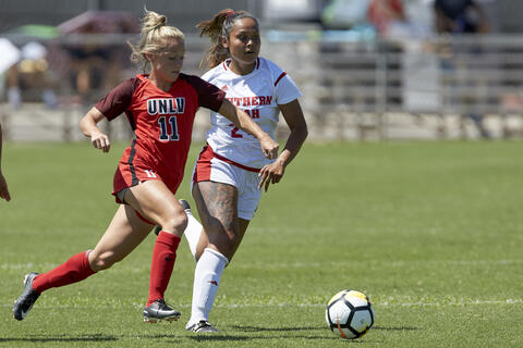 Two female soccer players going after the soccer ball on the field
