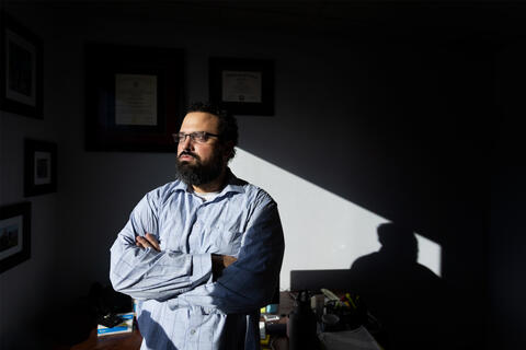 A man stands with his arms crossed looking out a window