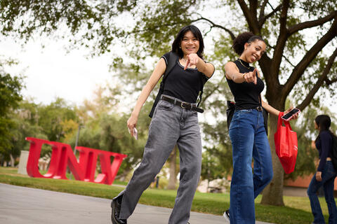 Two students walking together and pointing at the camera