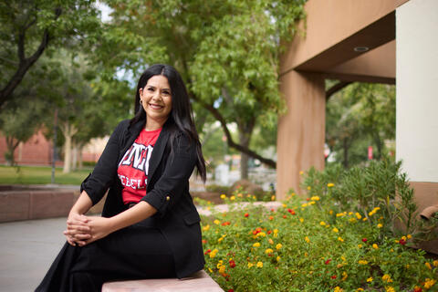 Mariella Bueno in black pants and jacket and red Rebels tshirt sits on a campus bench