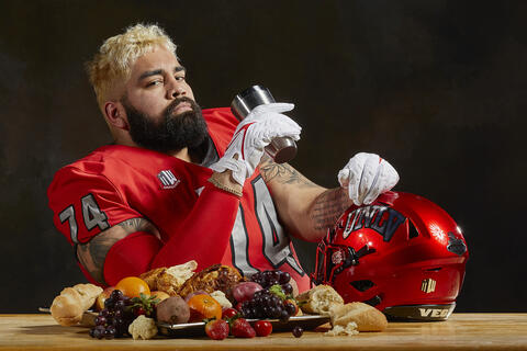 football player seated at dinner table with large plate of fruit and bread