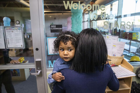 Woman carrying young child into preschool
