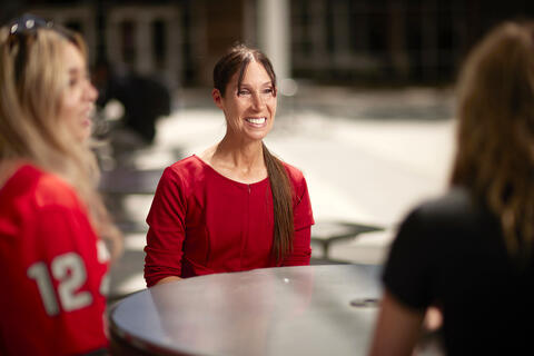 woman talking to two students around an outdoor table