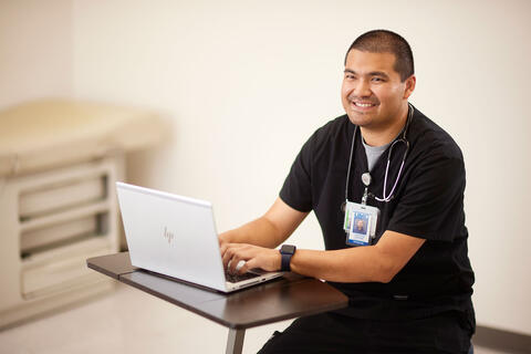 Julpohng (“JP”) Vilai, MD smiles while using laptop.