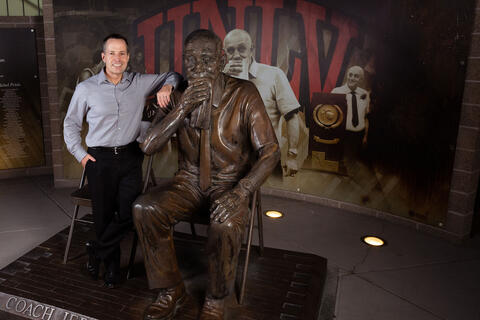 man posing at large outdoor statue of coach Jerry Tarkanian