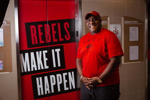 man standing in front of "rebels make it happen" banner