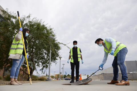 Members of the Precision Medicine Lab lifting off a manhole cover to study wastewater
