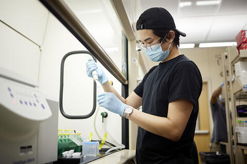Student in a lab working with tools to pipe material into a small vessel. 