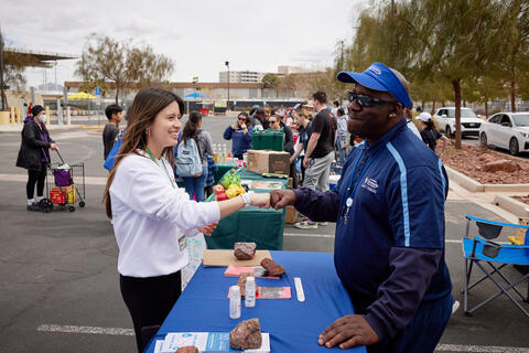 young female student bumping fists with man behind table