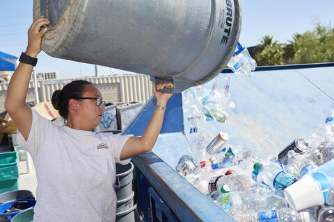 person emptying plastic recycling container into dumpster