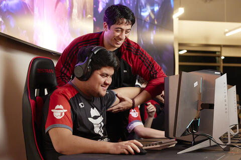 A student adjusts the arm of another student playing a computer game.