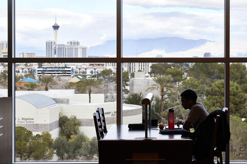 person working at desk in library with cityscape in view behind him