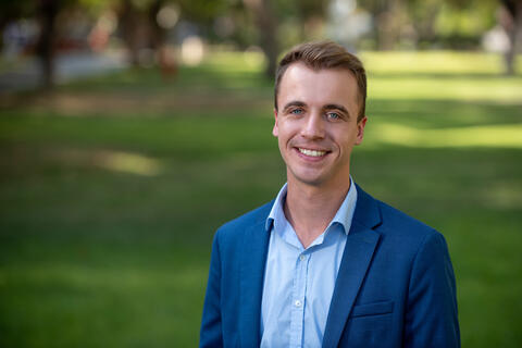 A man in a blue suit smiling in front of a grassy area.