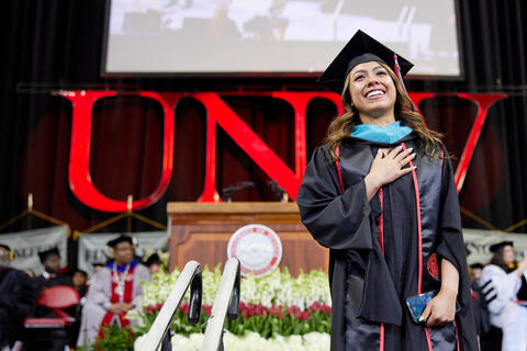 Graduate student on the stage of their commencement ceremony, staring into the crowd and smiling.