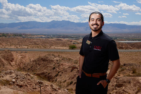 man stands in foreground with view of mountains and houses in background