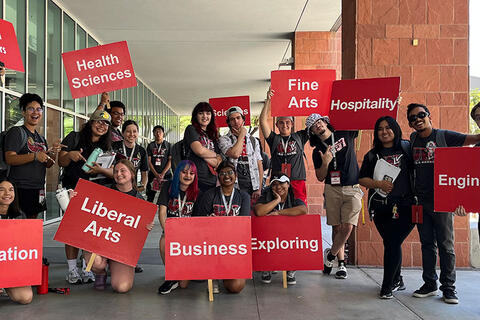 Urban Affairs, Health Sciences, Sciences, Fine Arts, Hospitality, Engineering, Education, Liberal Arts, Business, and Exploring majors holding up signs red signs with white text with the name of their schools.