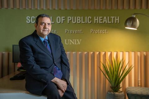 man in suit sits in front of wall that reads "school of public health"