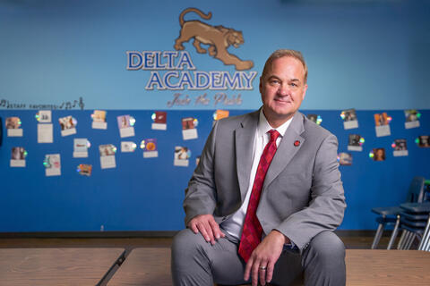 man sitting in front of wall that reads "delta academy"