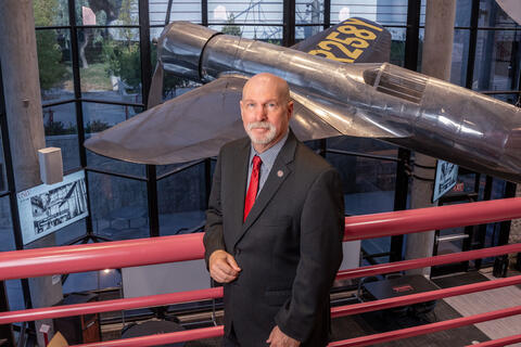 man standing by rail with plane in background