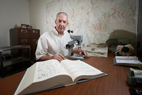 a man at a table with a microscope and open book