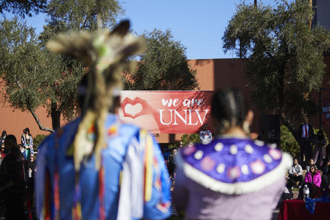 two blurred figures in Indigenous tribal dress on campus setting