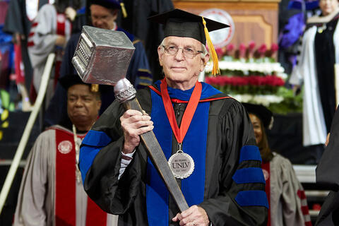 man in graduation robe carries mace during commencement
