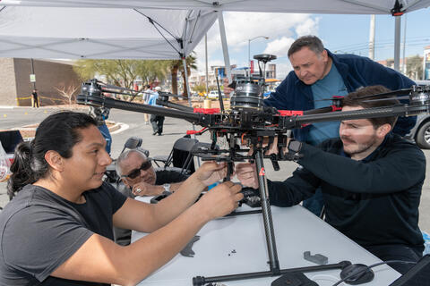 four men adjusting a drone before flight under popup tent