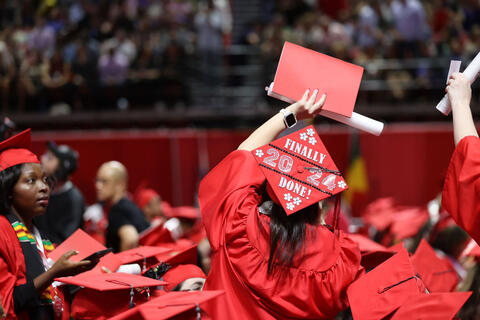 graduate in red regalia with decorated cap saying "Finally Done!"