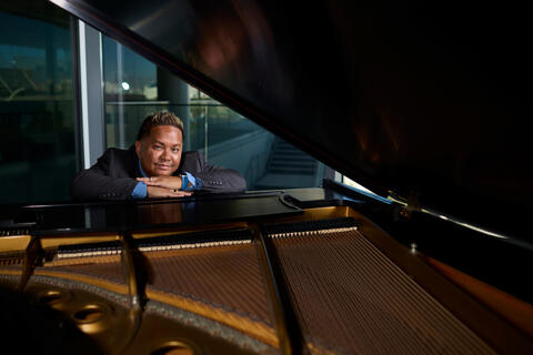 adeste sipin sitting at a black grand piano