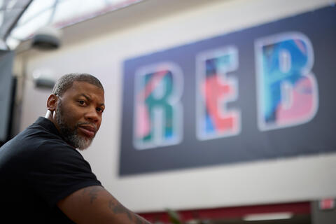 man looking to side with banner that reads 'REB' in the background