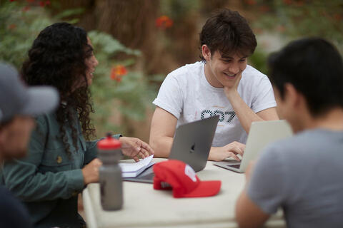 Four students hanging out on a table with their laptops