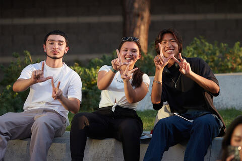 Three students using their fingers to form "L-V" letters for Las Vegas