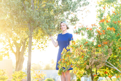 UNLV professor Alison Sloat in a blue dress outdoors underneath a tree with bright sun in the background
