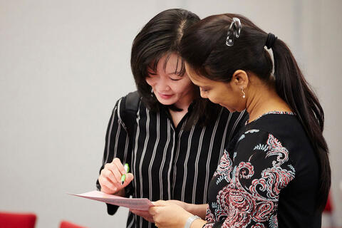 A instructor writing on a notebook with a student holding it
