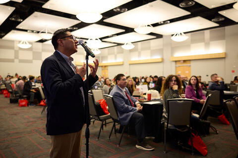 A man speaking in front of an audience in a ballroom
