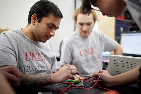 two people wearing gray shirts who are soldering wires in an electrical object