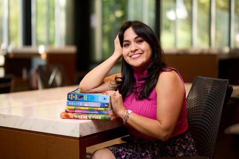 Kim Trevino poses in the Black Mountain Institute library with stack of books from past and present book club meetings