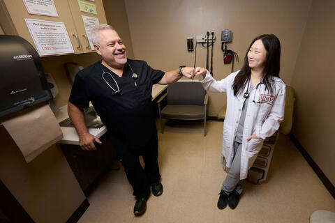two people in medical attire in exam room fist bumping