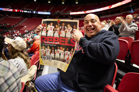 man at basketball game holding a Lady Rebels poster