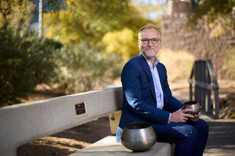 Brett Navziger on an a bench outside holding small metal pottery
