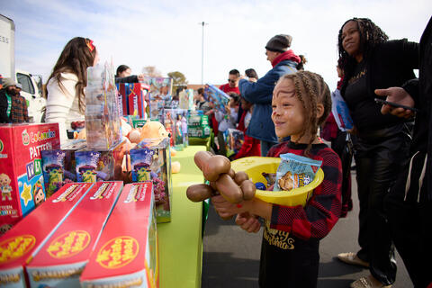 girl holding firehat and balloon animal looking at a table of toys