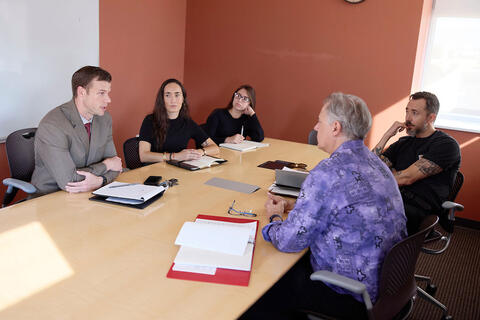 Five people sitting down at a table, have a discussion