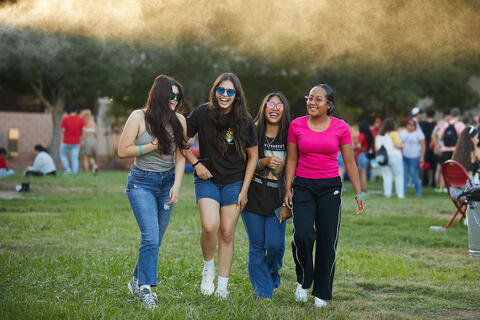 Four women linking arms and walking on grass
