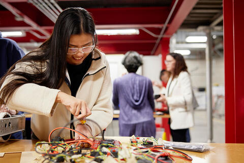A student wearing safety googles and a white lab working on a project