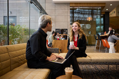 Two people in professional attire talking to each other on a lobby sofa